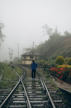 A person walking alone on misty railway tracks amidst lush surroundings in Sri Lanka.