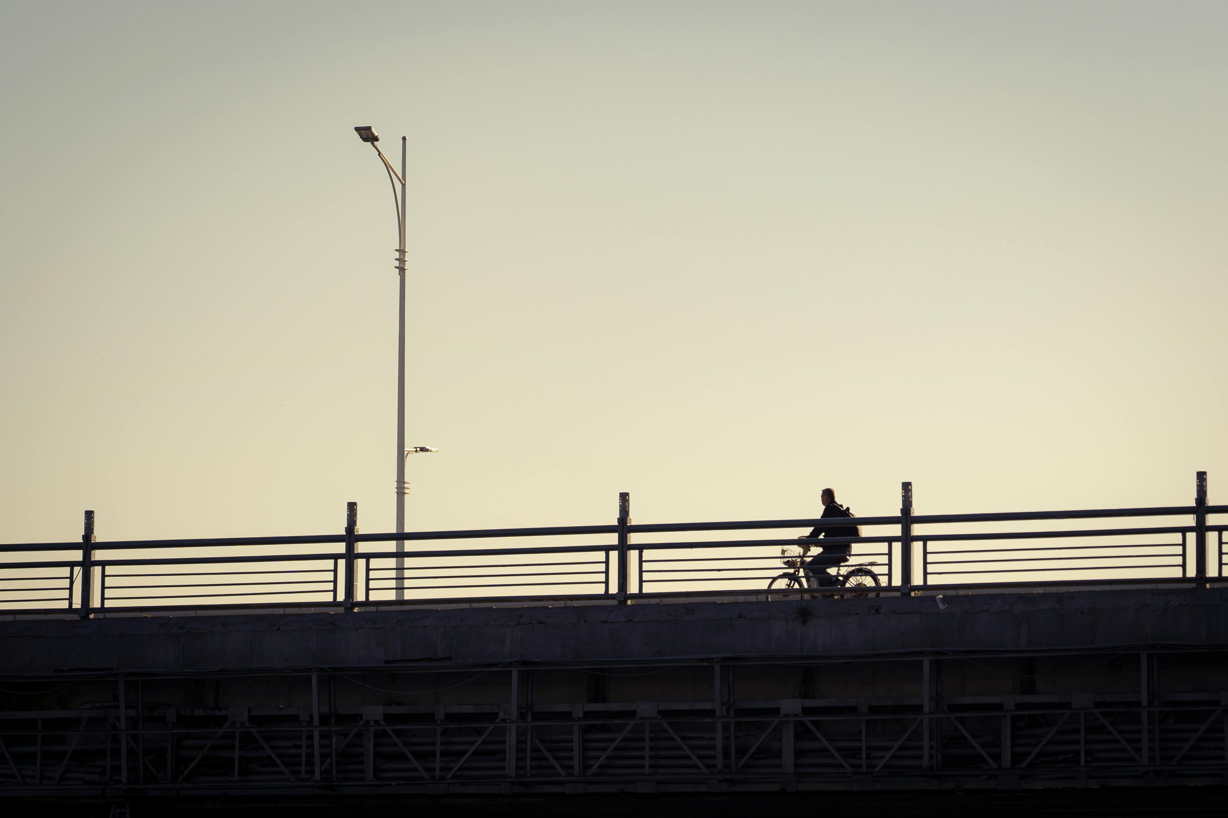 Silhouette of a person cycling on a bridge at sunset, evoking freedom and tranquility.