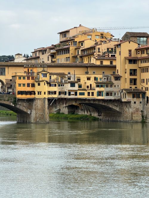 Free Scenic view of Ponte Vecchio in Florence reflecting in serene water under a cloudy sky. Stock Photo
