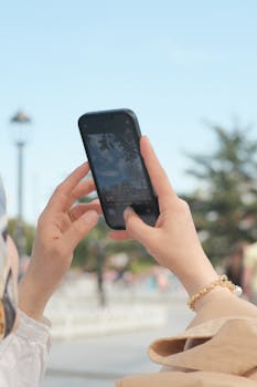 Close-up of a person capturing outdoor scene with a smartphone under blue skies.