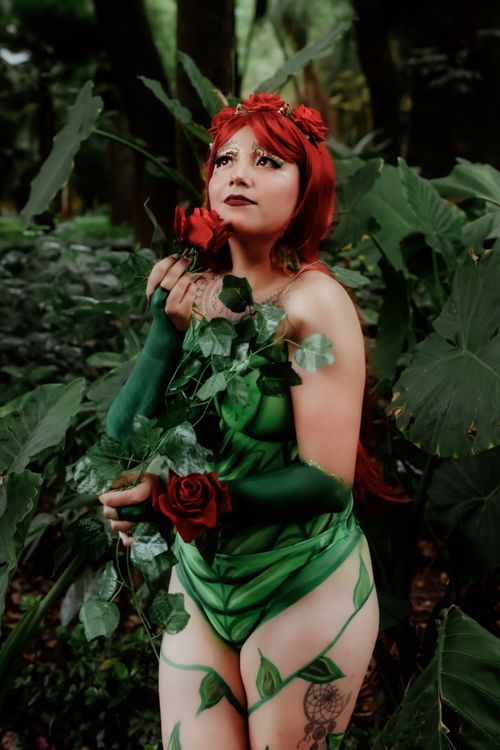 Free A vibrant cosplay portrait featuring a woman dressed as a plant-inspired character with red hair and roses, set in a lush garden. Stock Photo