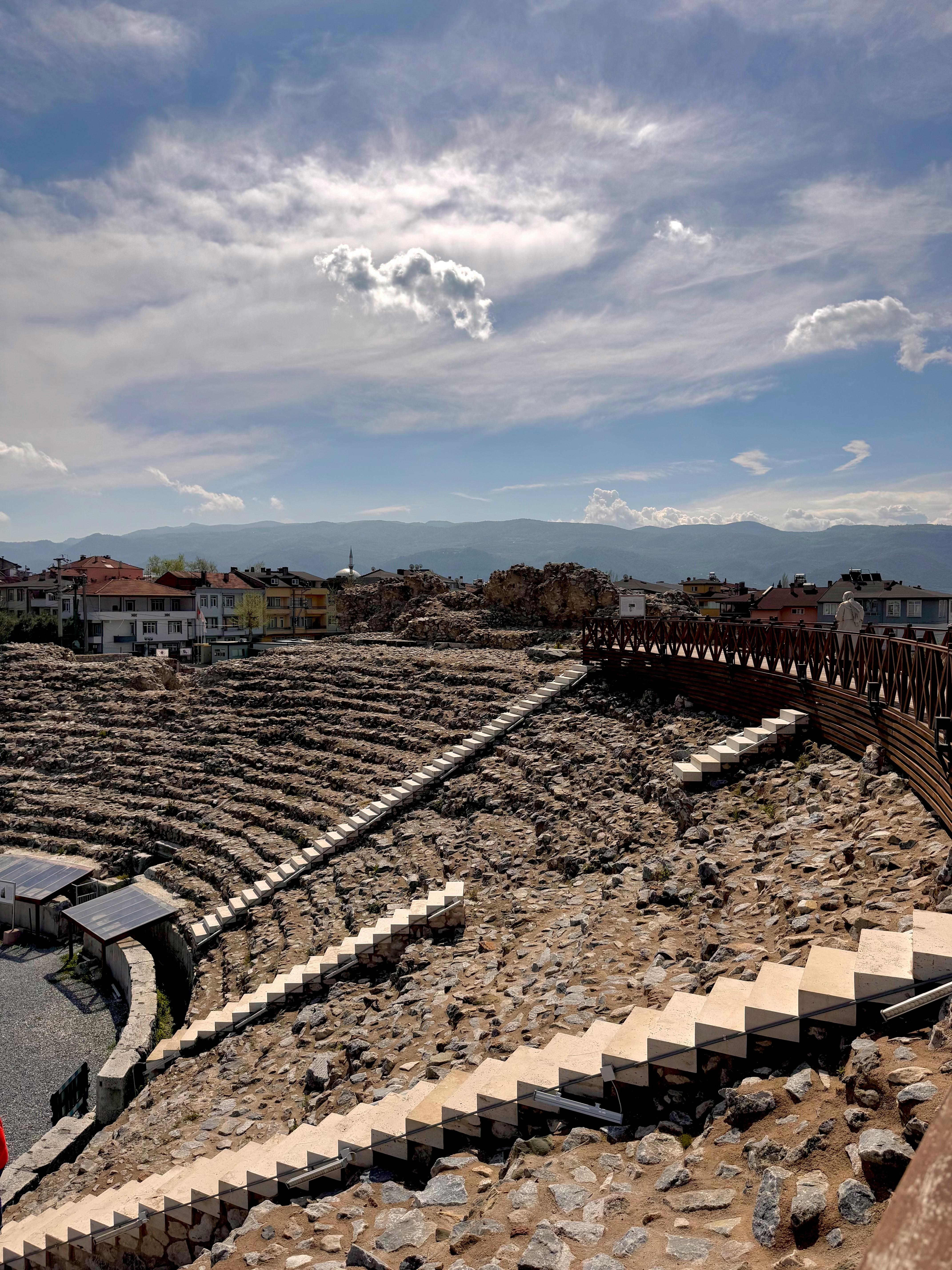 Kostenlos Atemberaubender Blick auf die Ruinen eines antiken römischen Amphitheaters mit dramatischen Wolken und einem klaren Tageshimmel. Stock-Foto