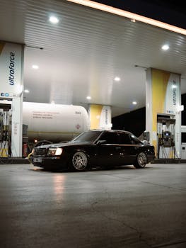 A sleek black car refueling at a gas station under bright lights during nighttime.