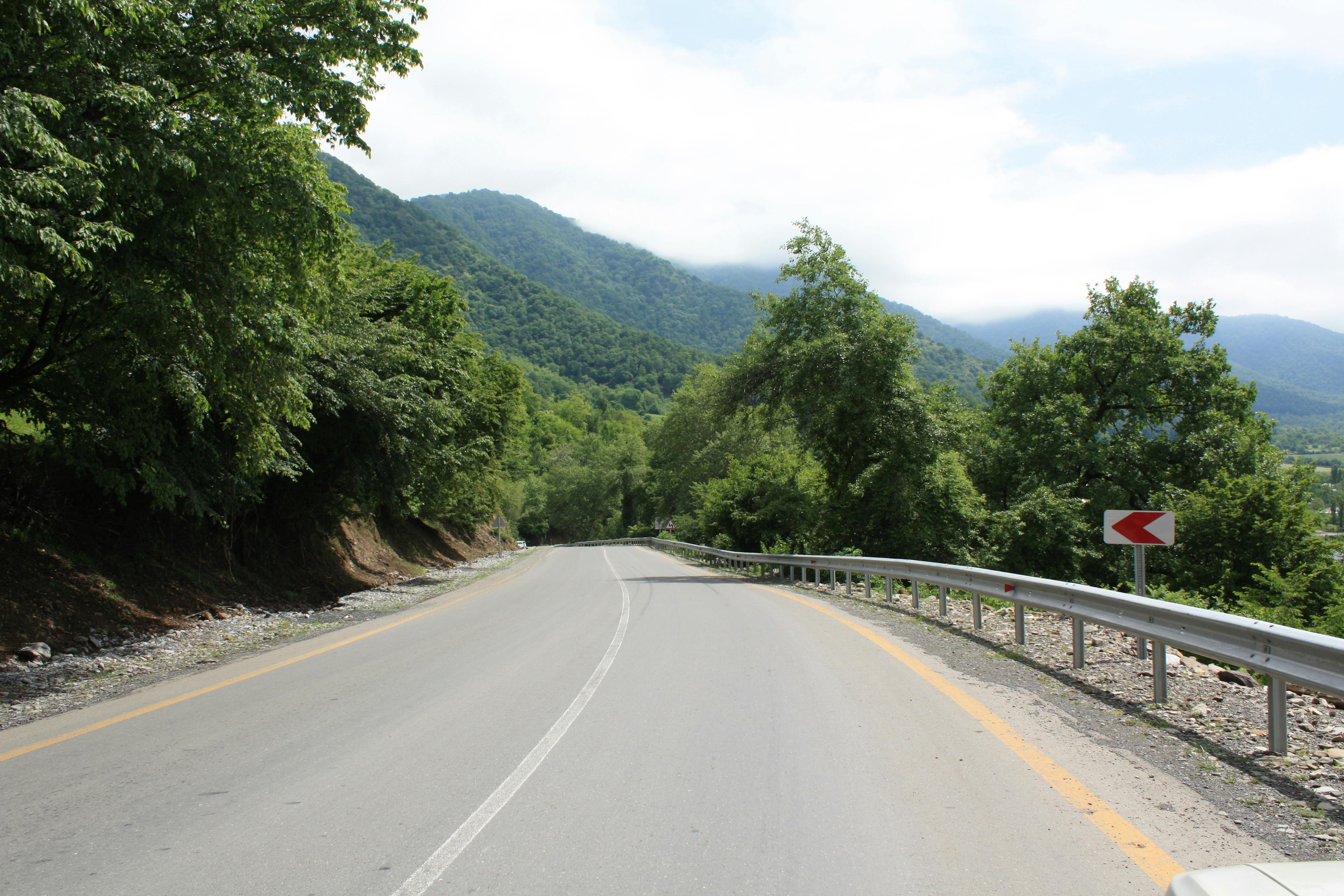 A peaceful winding road through a lush, green mountainous landscape on a sunny day.