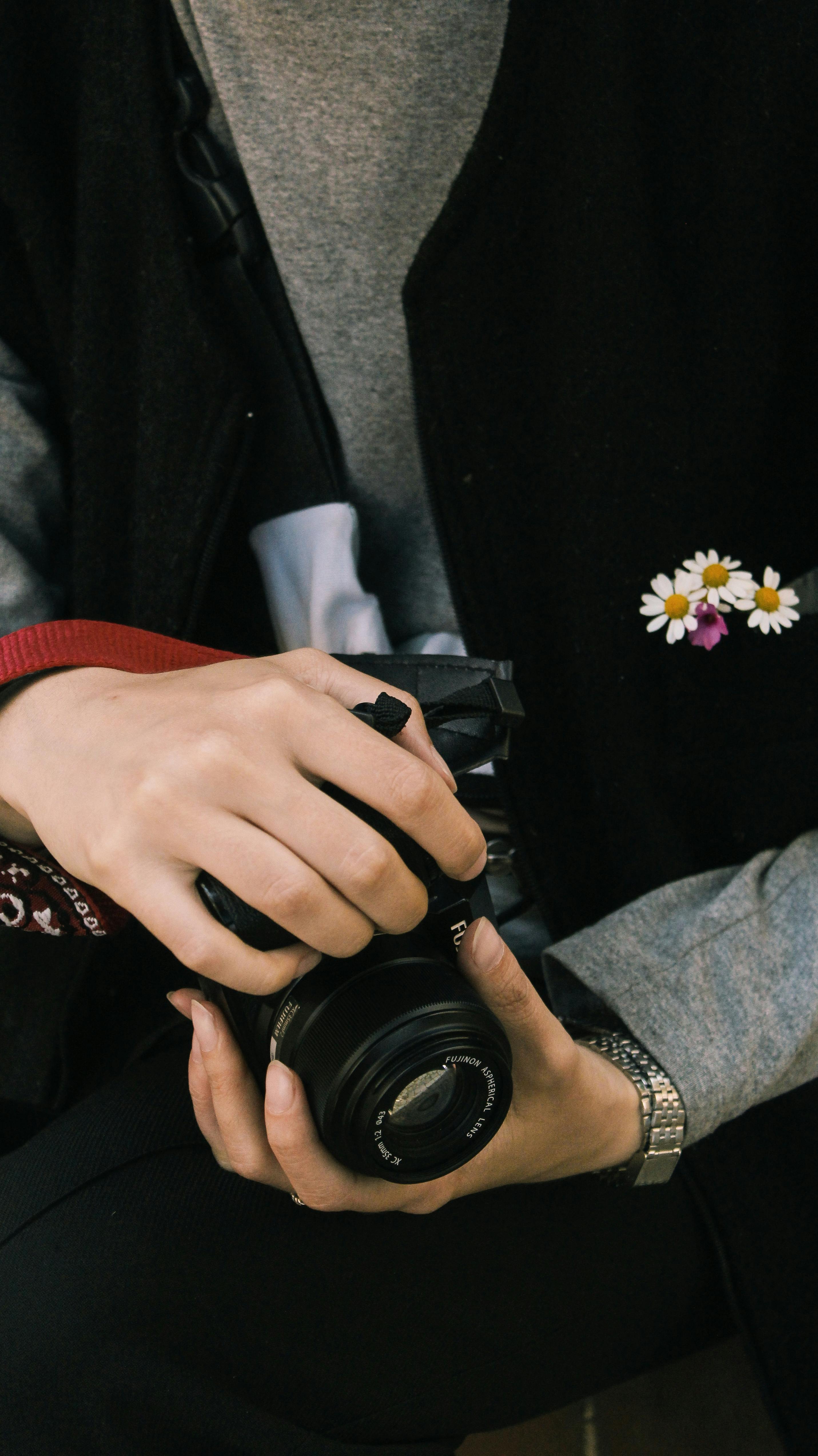 Close-up of a person's hands holding a camera with flowers in pocket, artistic vibe.