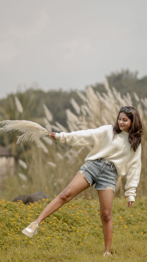 Free Young woman posing in a field with tall grass, creating a playful and natural vibe. Stock Photo