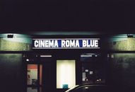 Neon-lit sign of Cinema Roma Blue in Turin, Italy at night showcasing retro aesthetic.