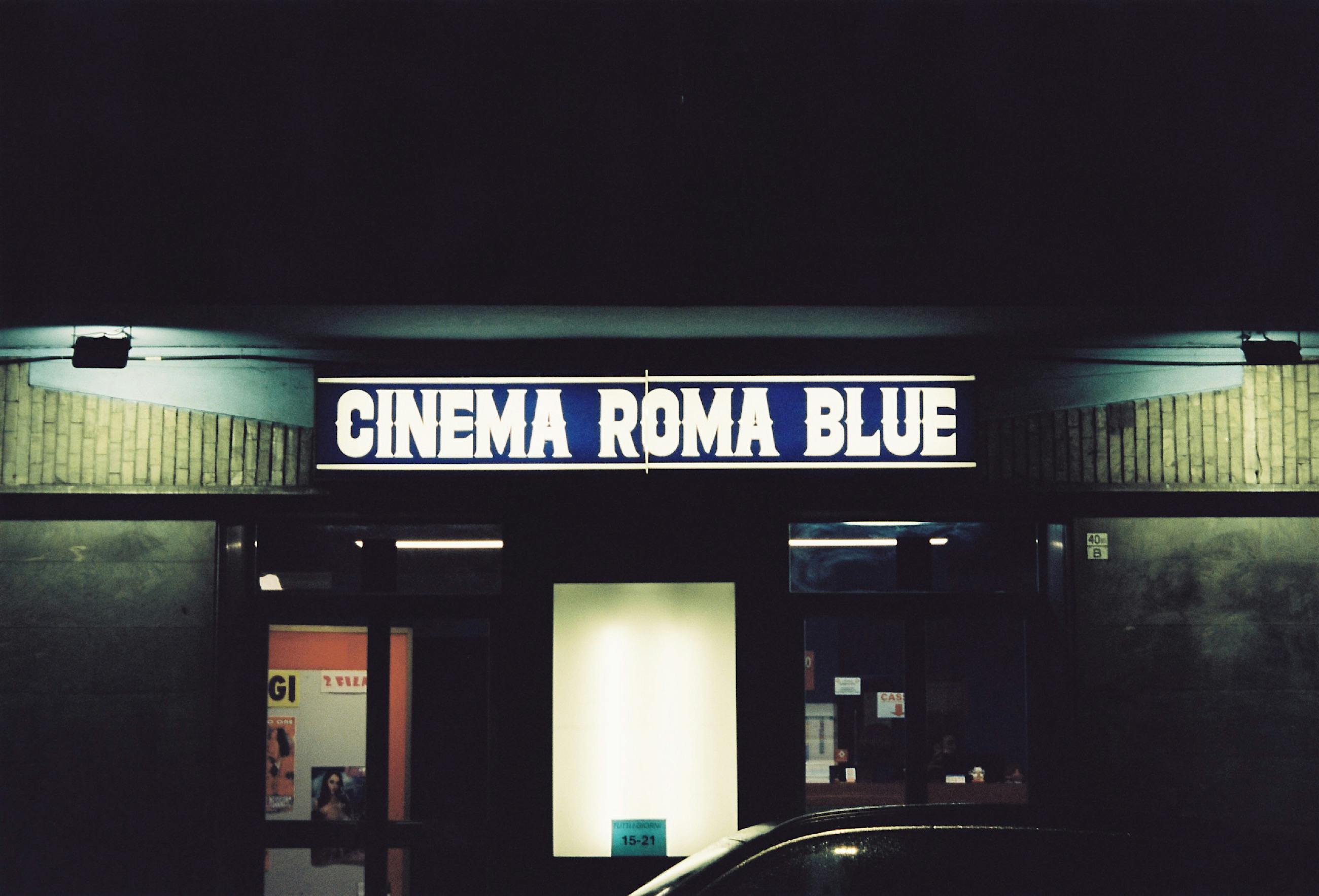 ฟรี ป้ายนีออนของร้าน Cinema Roma Blue ในเมืองตูริน ประเทศอิตาลี ในเวลากลางคืน แสดงให้เห็นถึงความงามแบบย้อนยุค คลังภาพถ่าย