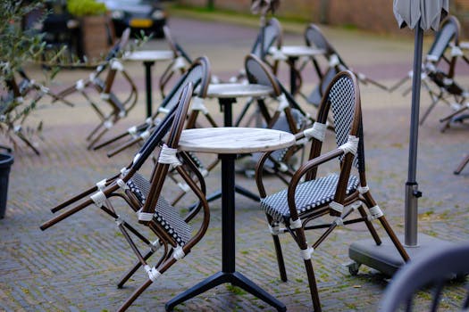 Empty patio tables and wicker chairs on a cobbled terrace in Amsterdam.