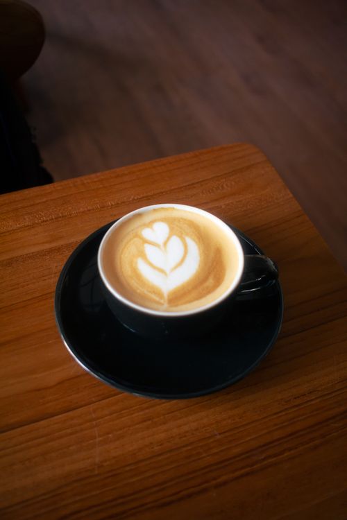 Free A beautifully crafted latte with heart-shaped art served in a black cup on a wooden table. Stock Photo