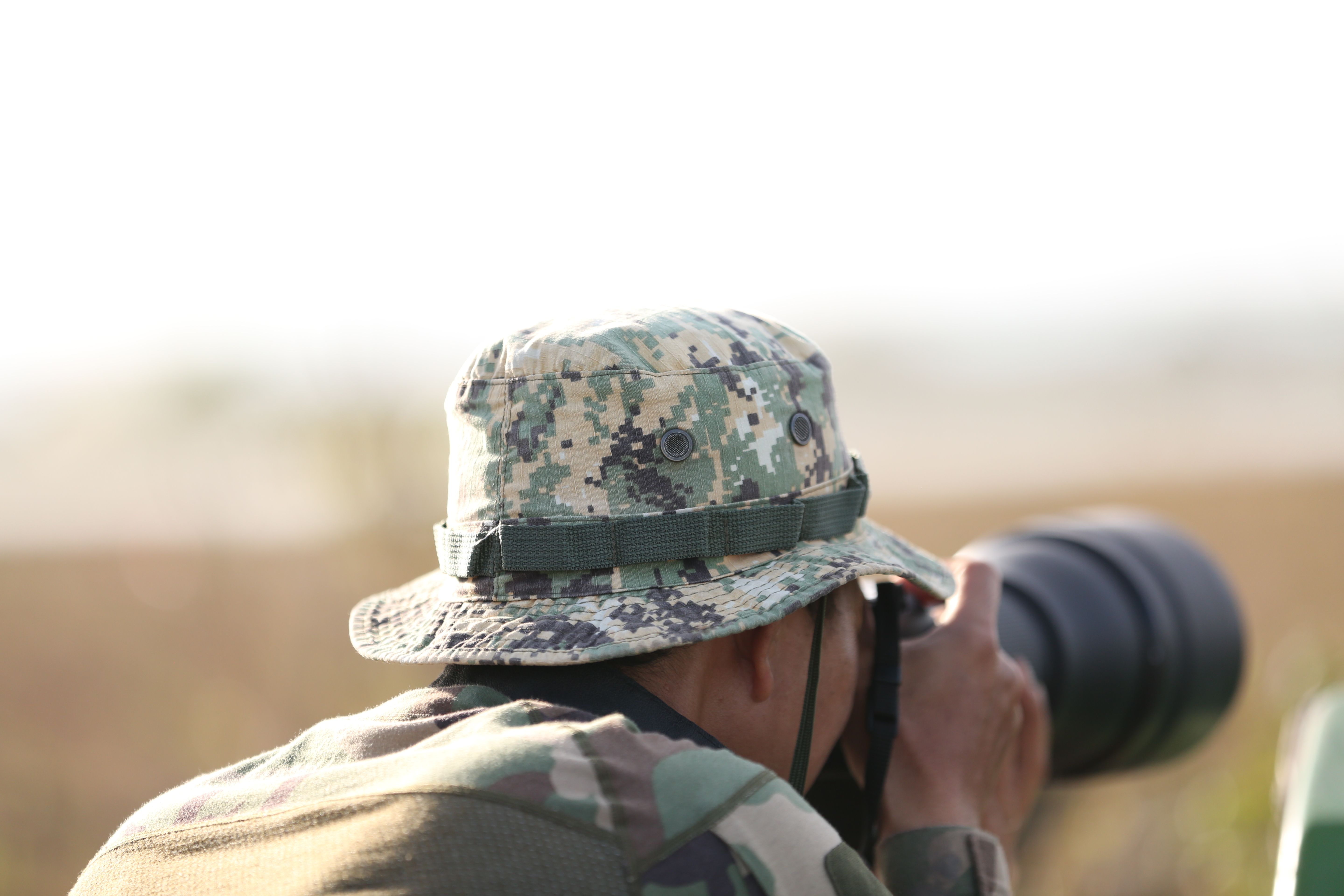 Yapay Zeka Gözetimini Kandıran Gömlek: Dijital Kamuflaj Devrimi Mi? - A wildlife photographer wearing camouflage gear captures images outdoors with a telephoto lens.