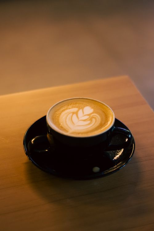Free Close-up of a beautifully crafted latte with art in a black cup on a wooden table in soft lighting. Stock Photo
