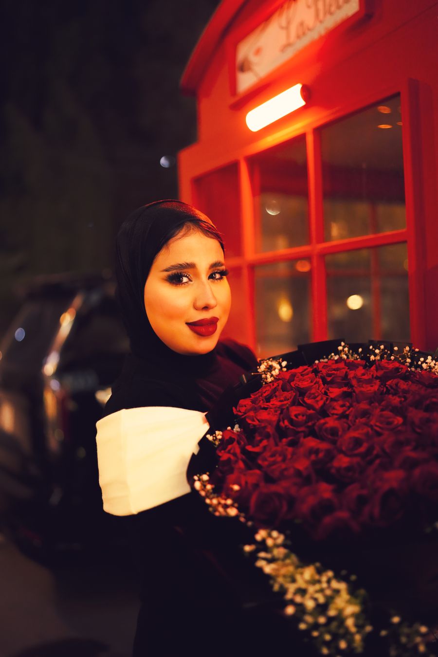 A woman smiling next to a large bouquet of red roses