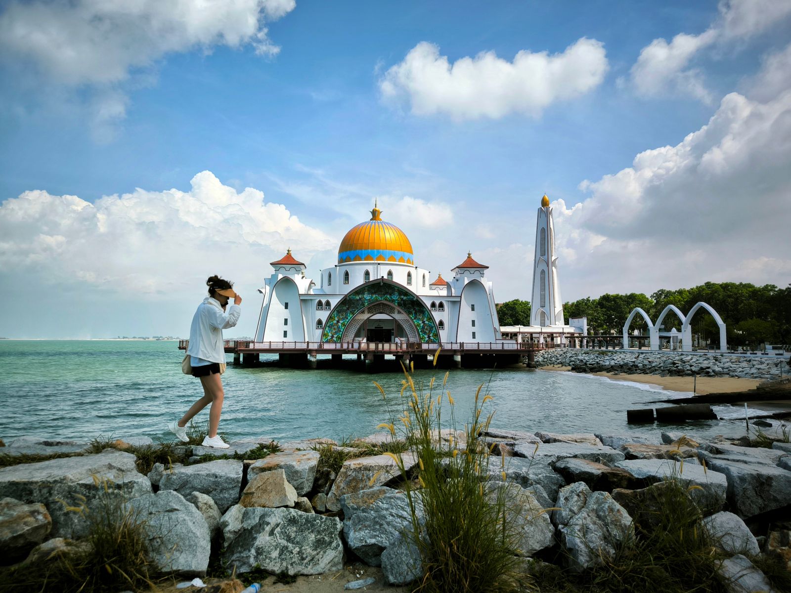 A person walking near the picturesque Malacca Straits Mosque with a clear blue sky in the background.