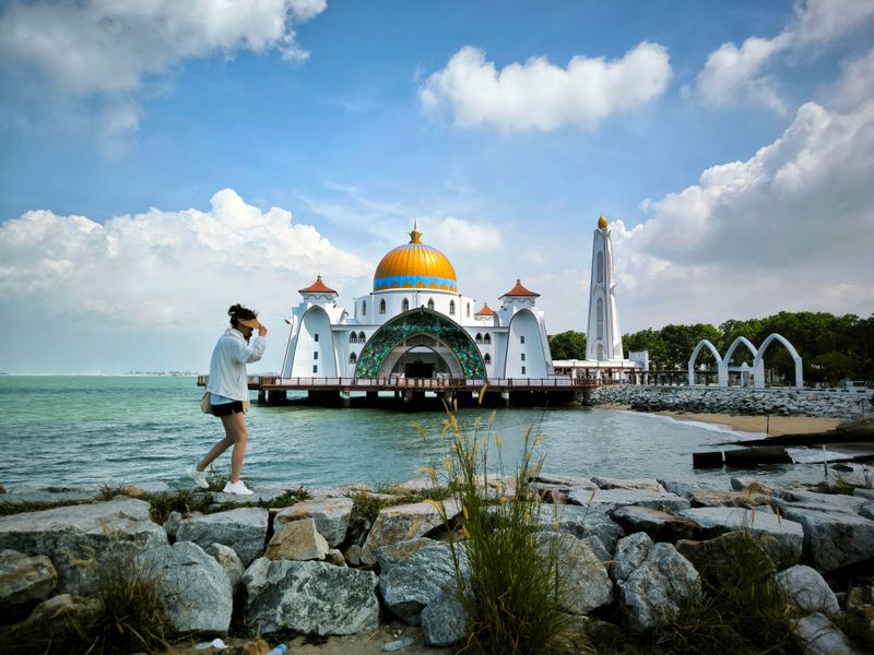 A person walking near the picturesque Malacca Straits Mosque with a clear blue sky in the background.