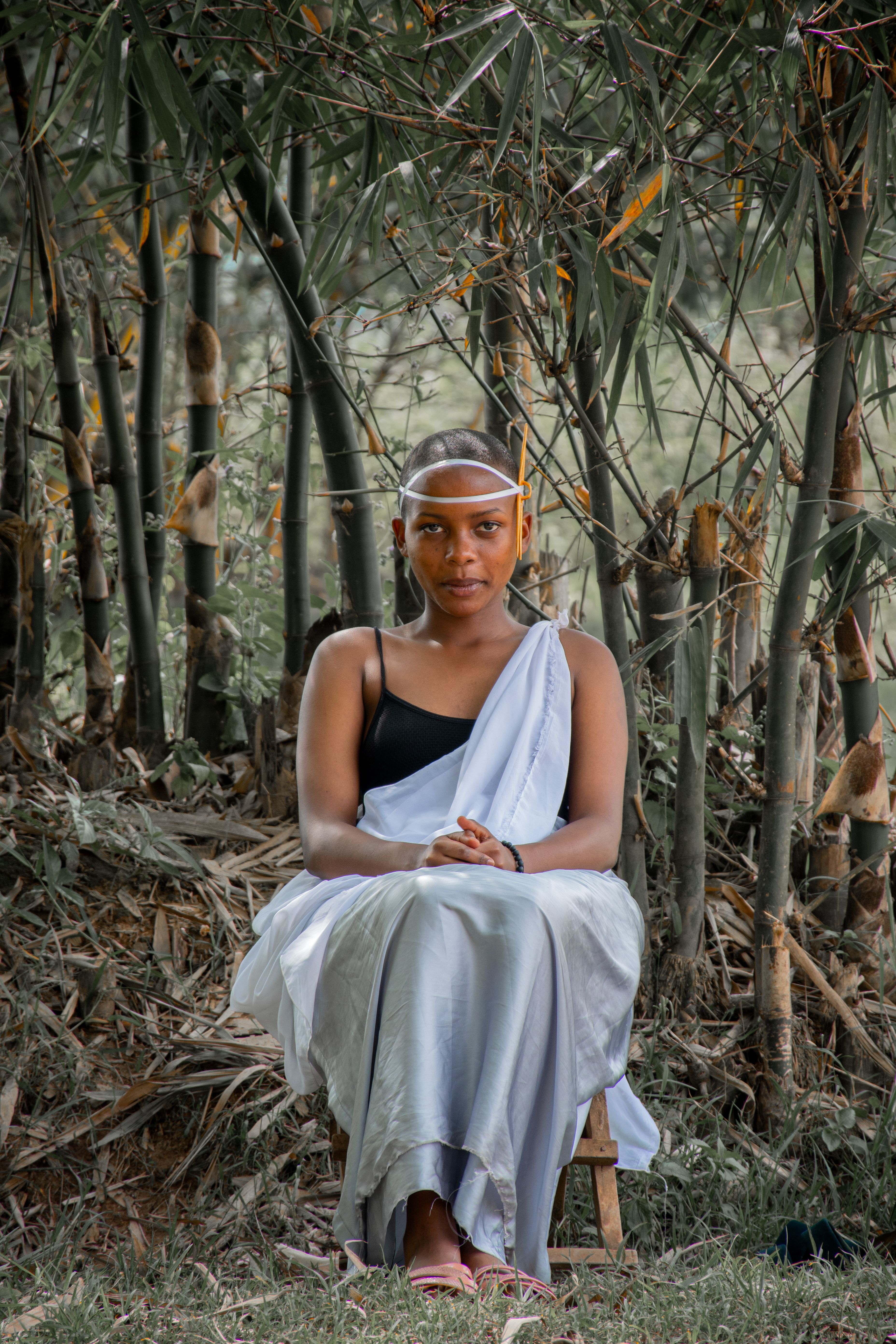 A woman in traditional attire sits gracefully in front of bamboo, showcasing cultural elegance.
