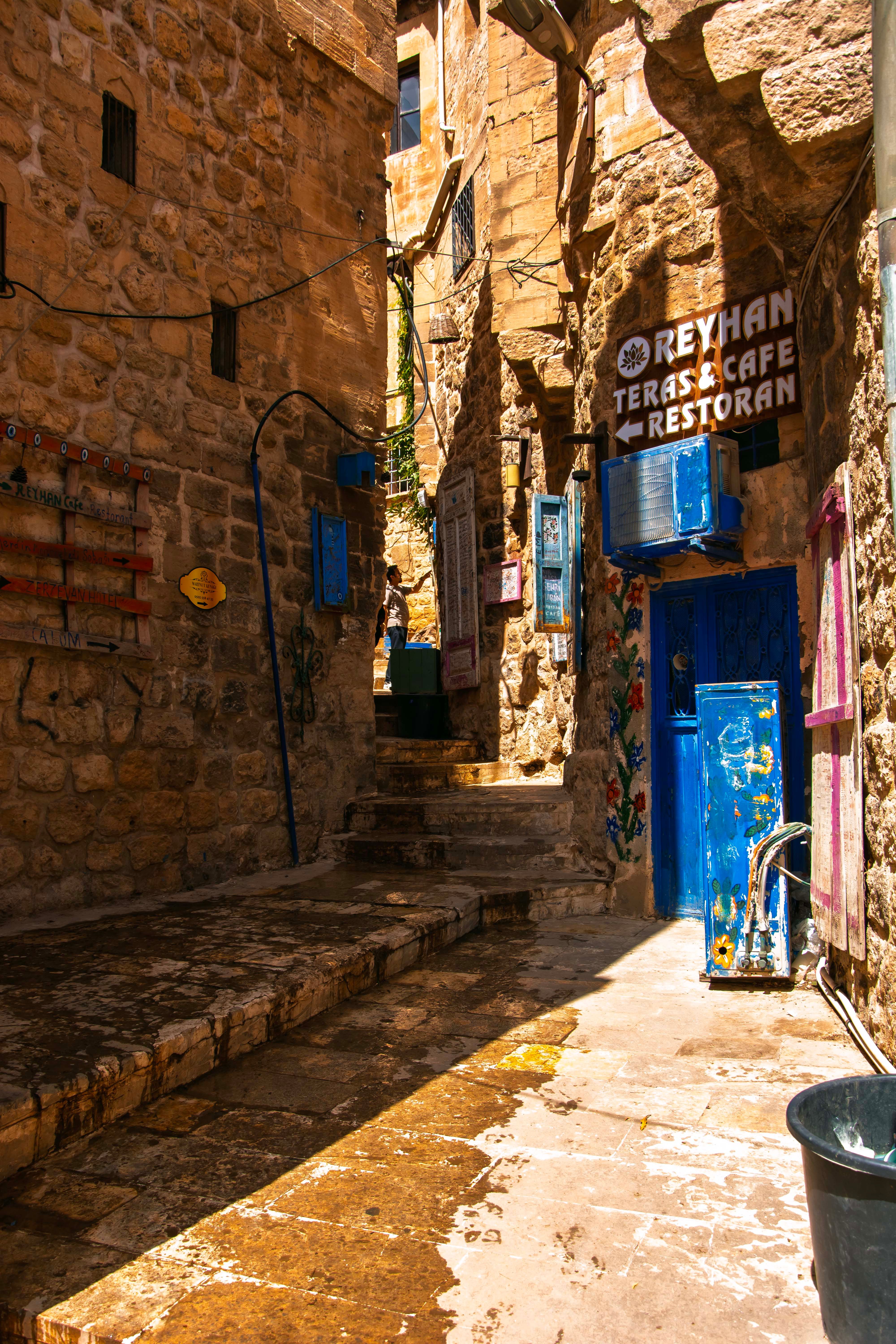 Sunny day view of a narrow stone alley in Mardin, capturing historical architecture and colorful accents.