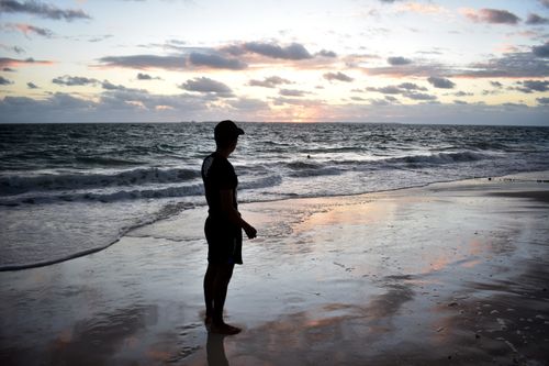 Free A solitary figure stands on the shore at sunset, reflecting serenity and contemplation. Stock Photo