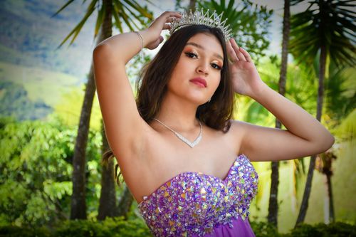 Free Elegant young woman in purple dress and crown posing outdoors surrounded by greenery. Stock Photo