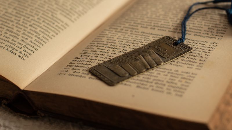 Geprägtes Metall-Lesezeichen mit blauer Kordel liegt auf einem aufgeschlagenen alten Buch in Frakturschrift