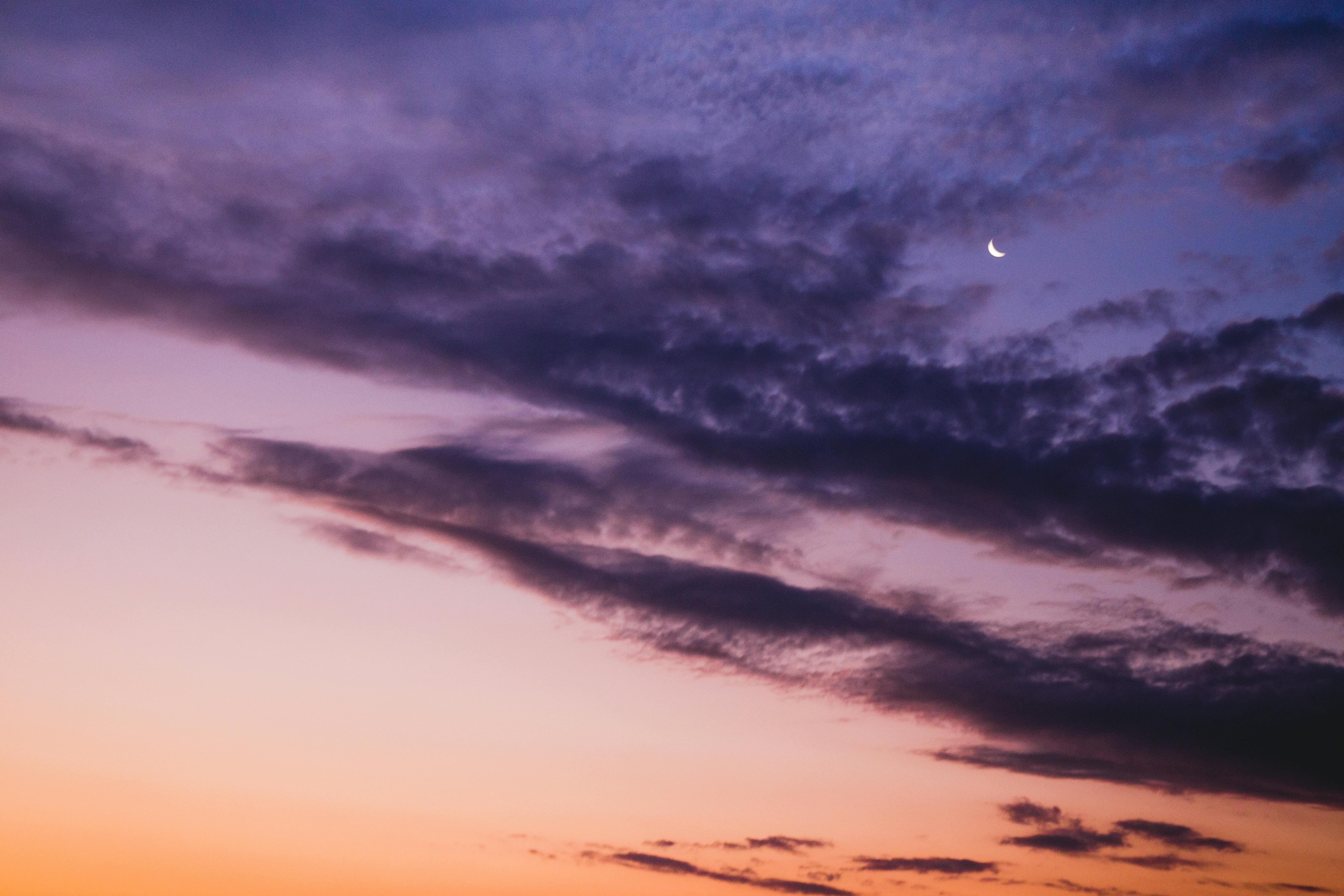 A serene purple sky with a crescent moon and dramatic cloudscape at twilight.