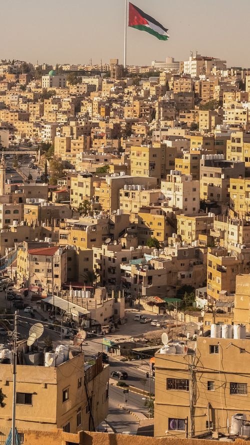 Free Panoramic view of Amman city with the iconic Jordanian flag fluttering, highlighting its urban landscape. Stock Photo