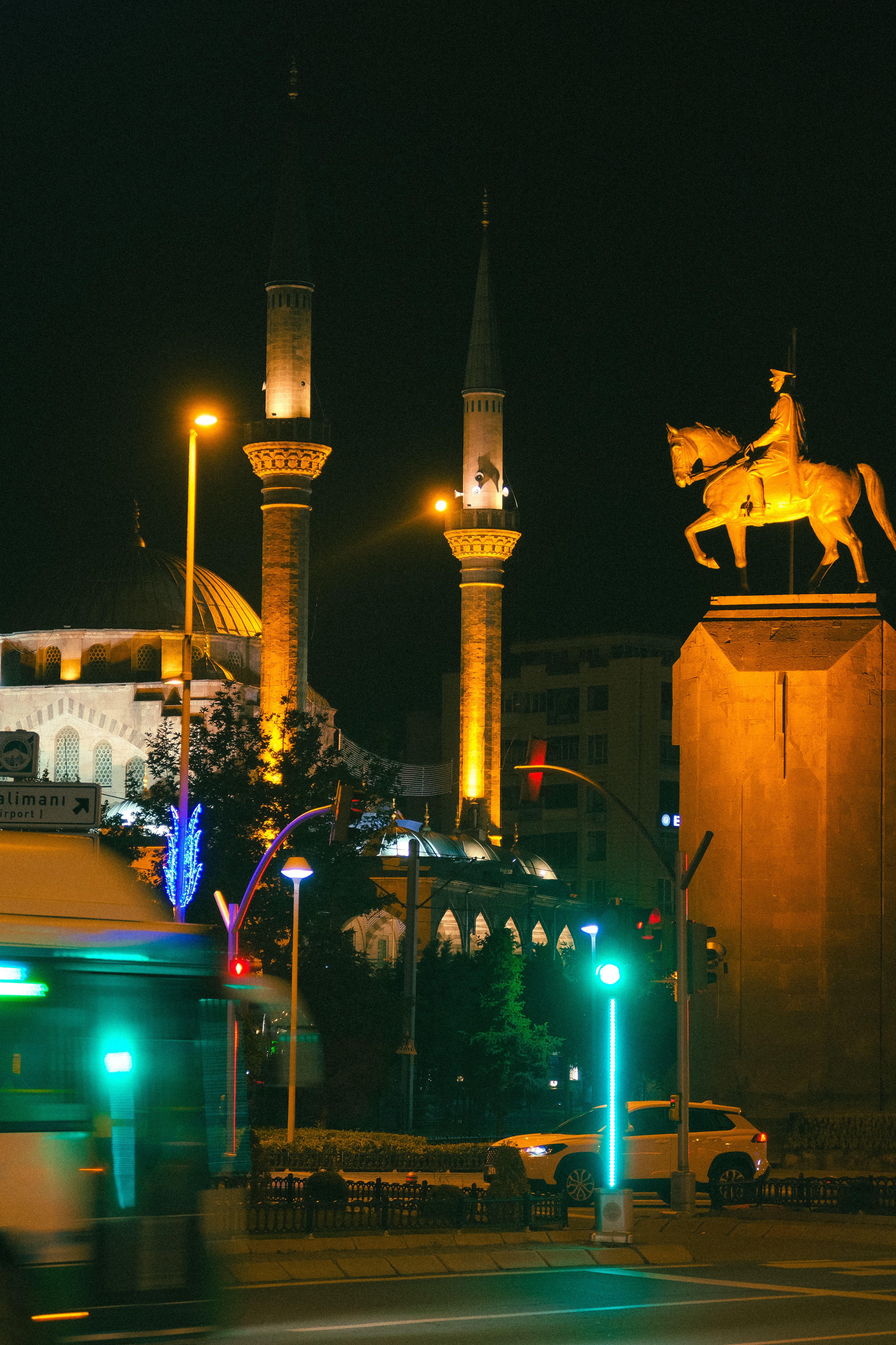 Night view of an illuminated mosque and equestrian statue, city lights around.
