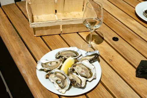 Free Plate of fresh oysters with a lemon wedge and wine glass on a wooden table outdoors. Stock Photo