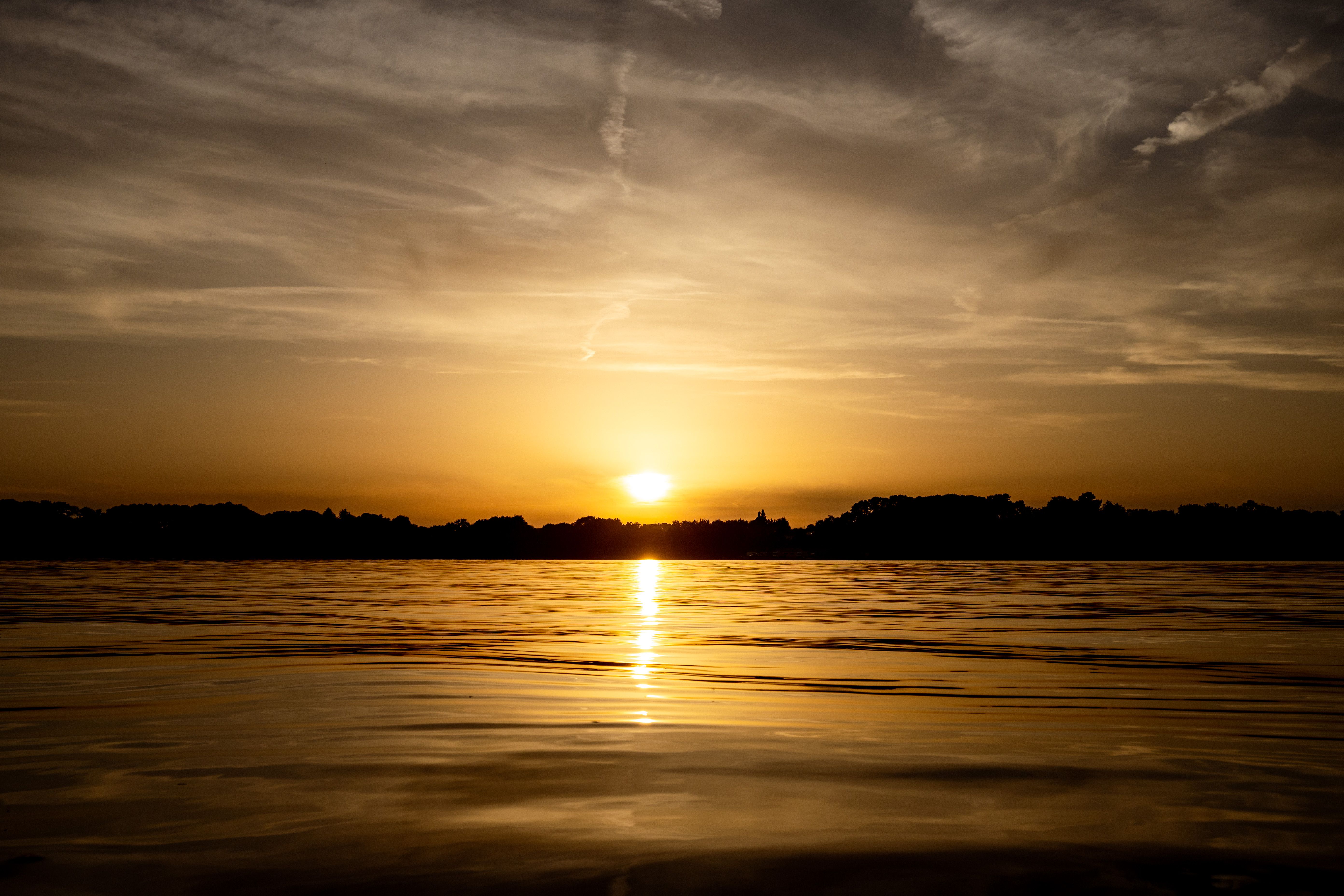 Gratis Matahari terbenam yang indah terpantul di danau yang tenang dengan langit dan siluet yang dramatis. Foto Stok
