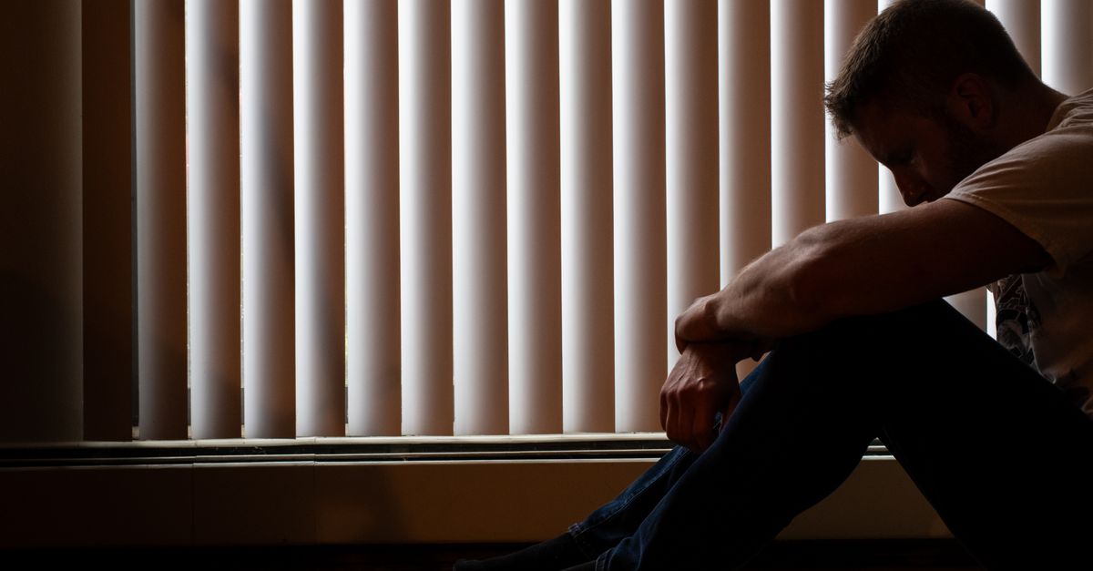 A man sits silhouetted against window blinds, conveying solitude and introspection. - Evidence evidence guide for probiotic depression randomized trial