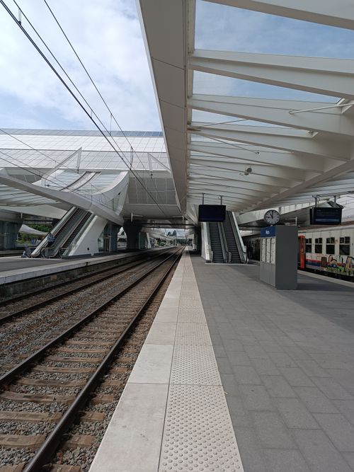 Free A spacious train station platform with unique steel architecture and empty tracks, captured during the day. Stock Photo
