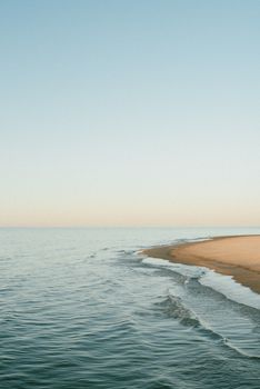 Calm sea waves gently meeting the sandy shore under a pastel sky at dawn, perfect for relaxation themes.