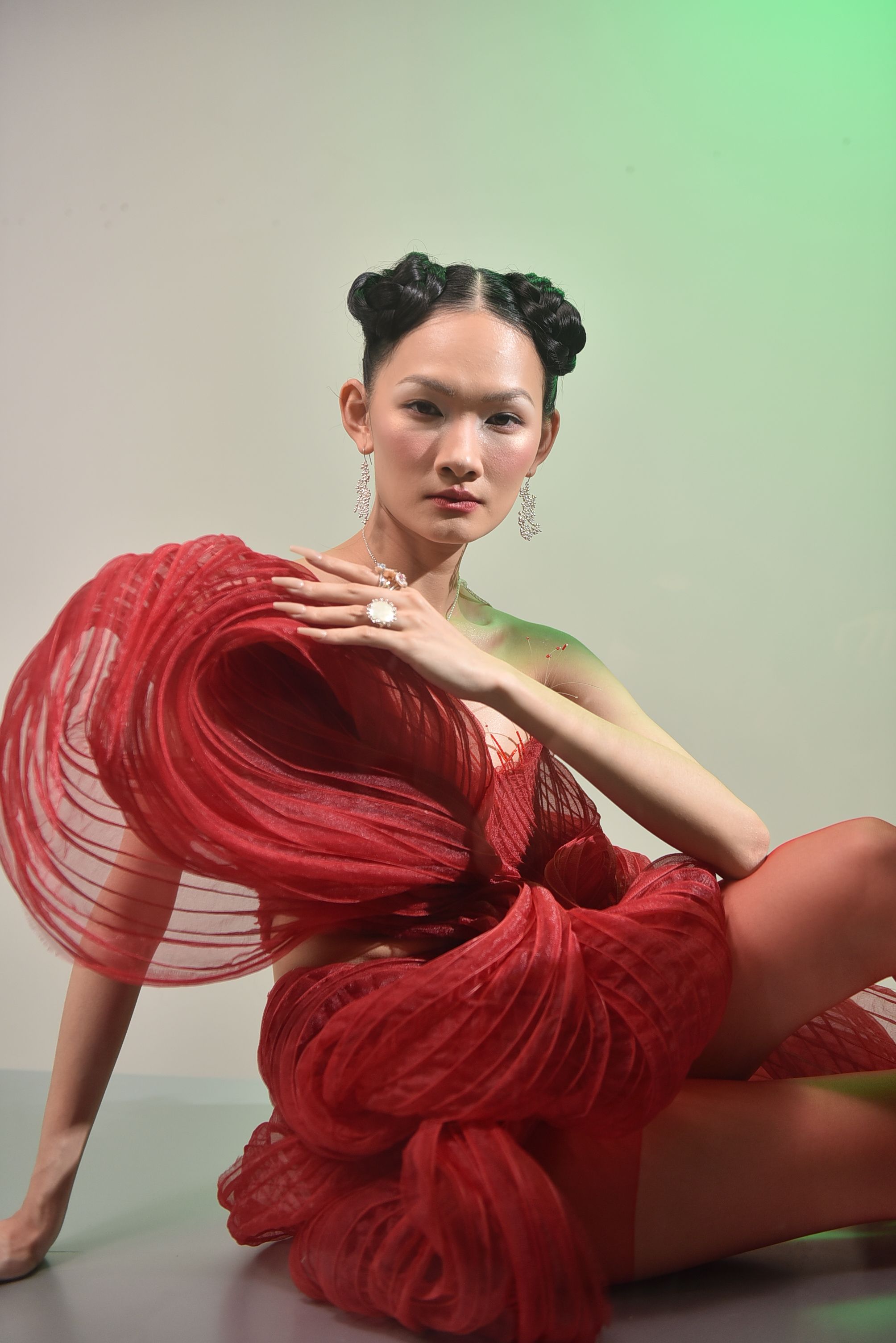 Model in an artistic red dress with unique design, sitting gracefully indoors.