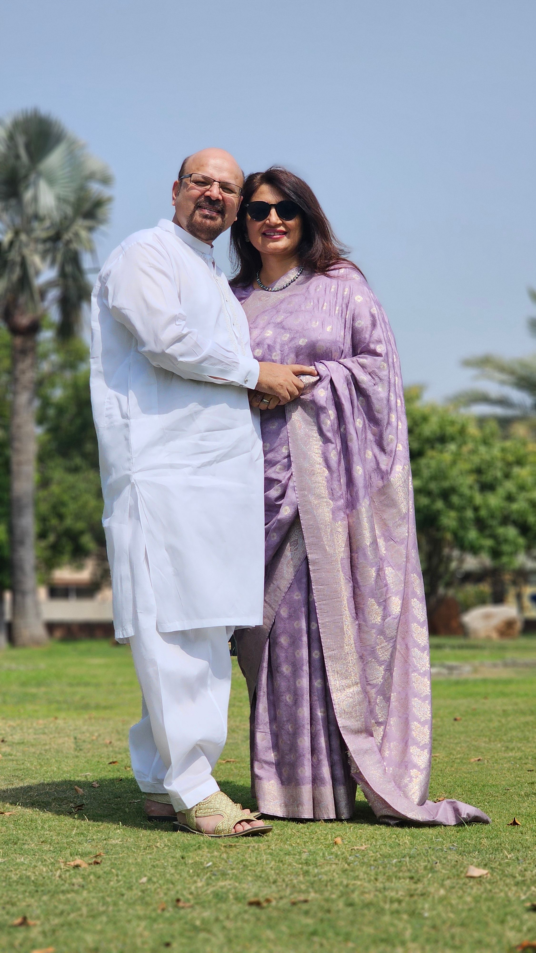 Smiling couple in traditional attire enjoying a sunny day outdoors.