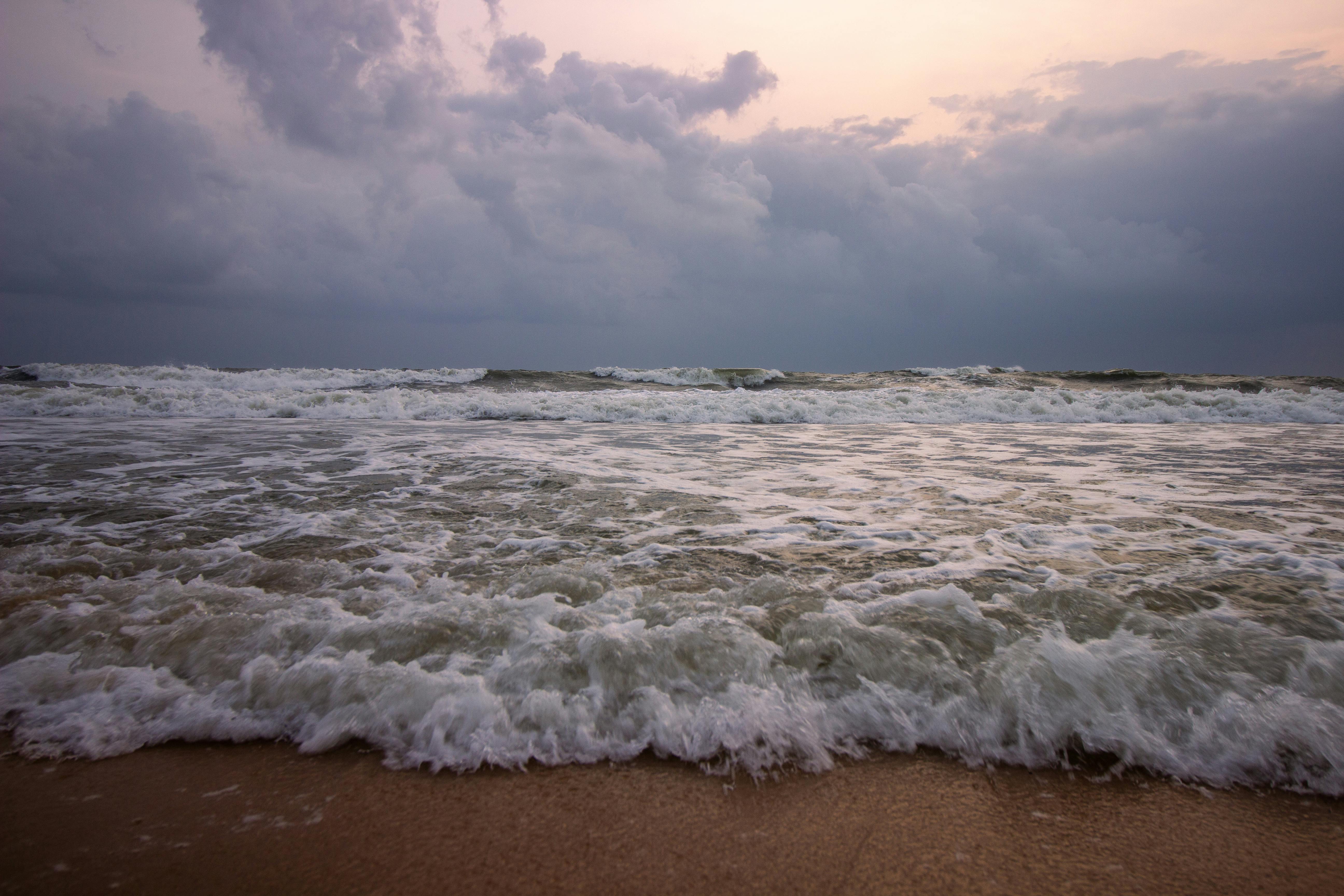 A serene beach scene with waves crashing on the shore under a dramatic sunset sky with storm clouds.