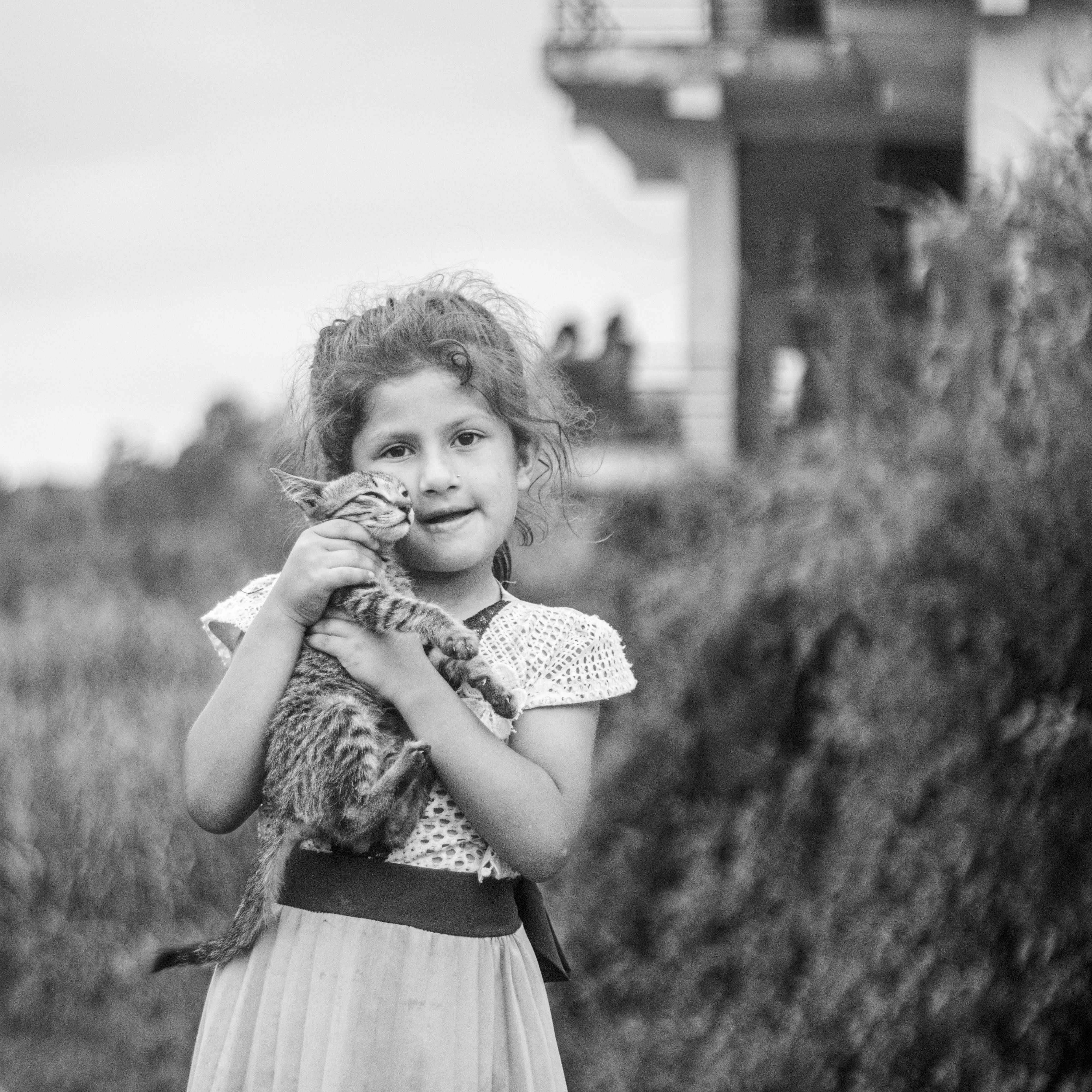 Heartwarming portrait of a young girl holding a kitten in a rural setting, captured in black and white.
