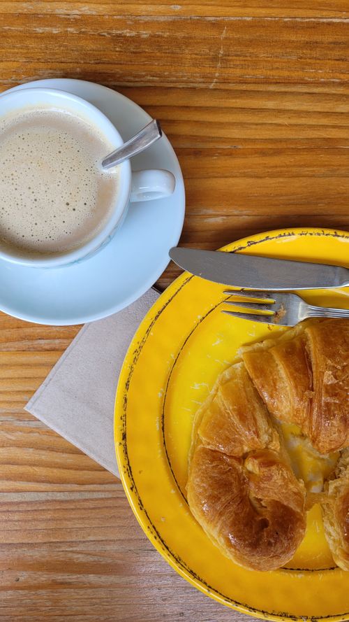 Free A cup of coffee with a buttery croissant on a vibrant yellow plate on a wooden table. Stock Photo