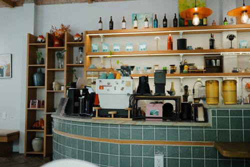 Free Cozy coffee shop interior featuring a green tile counter, espresso machine, and stylish decor. Stock Photo