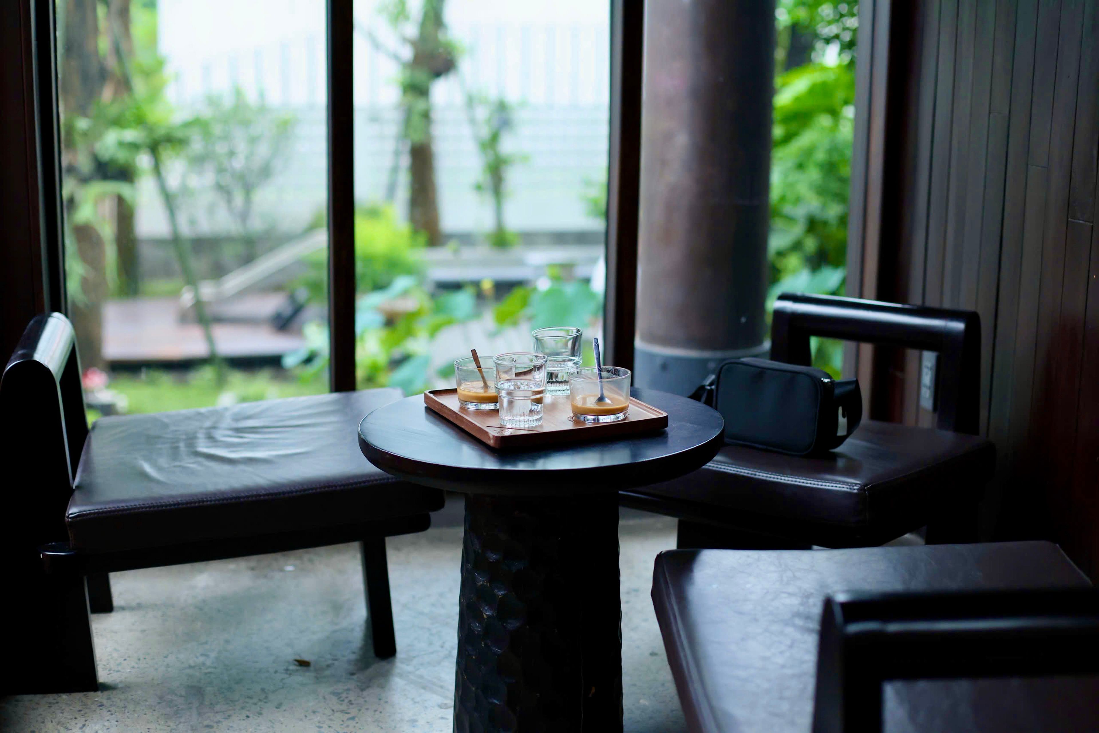 A tranquil indoor setting with a coffee table, leather chairs, and a garden view.