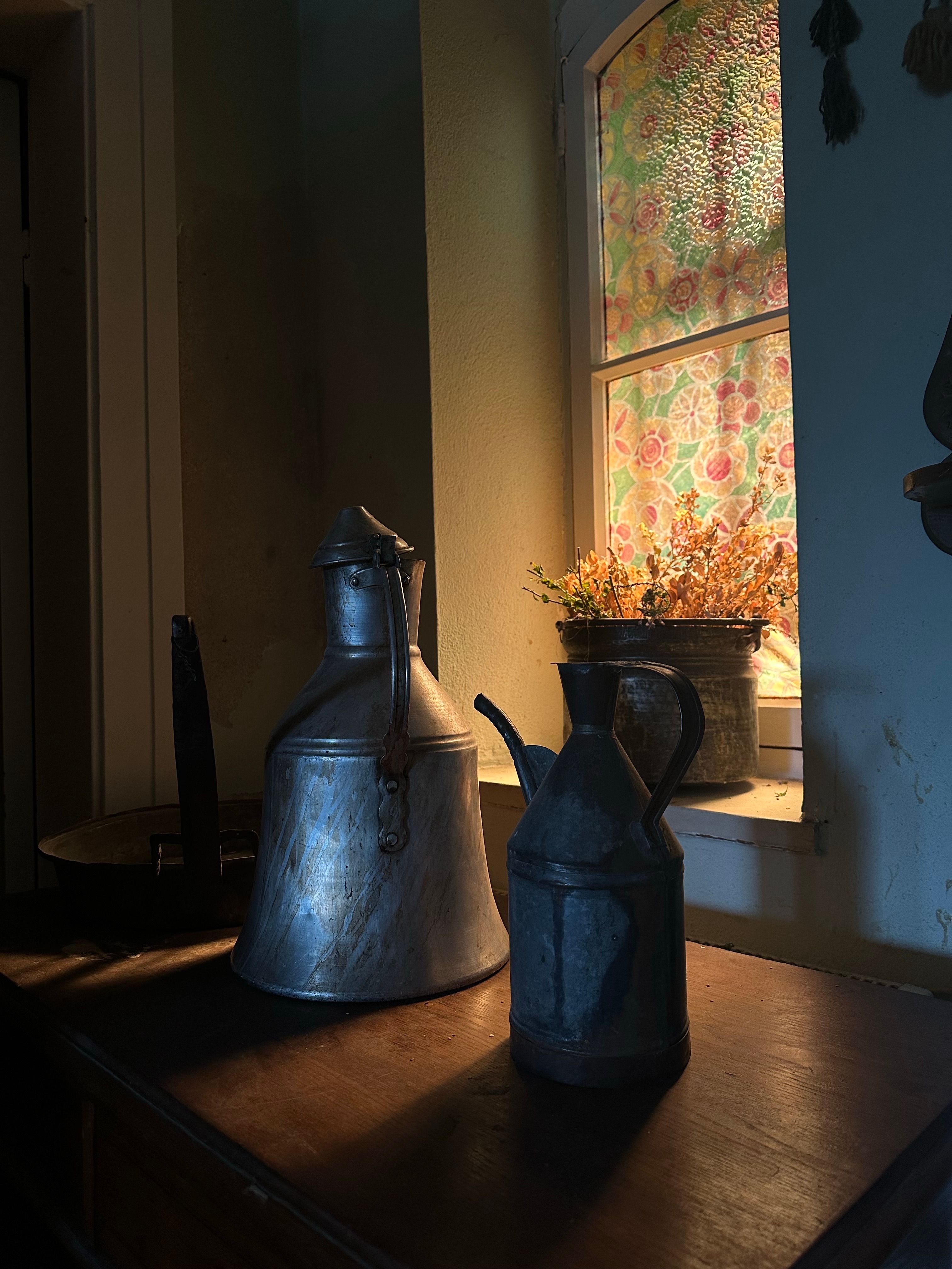 Rustic still life of vintage oil cans on a table by a stained glass window.