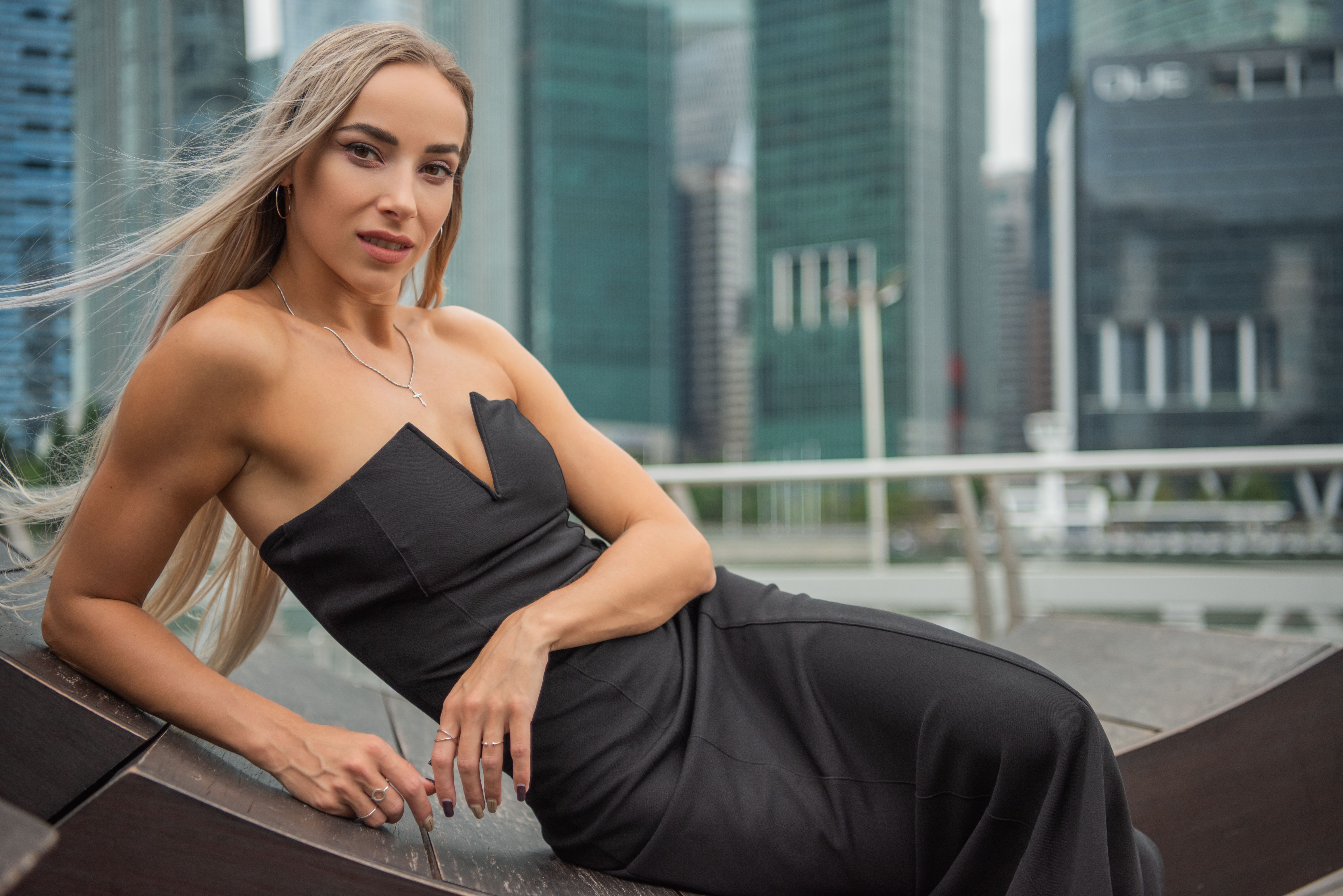 Stylish woman in black dress poses confidently with urban skyline backdrop.