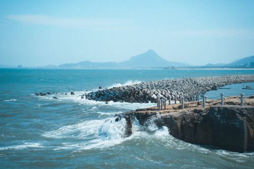 Free Stunning seascape with a protective breakwater and mountainous backdrop under a clear blue sky. Stock Photo