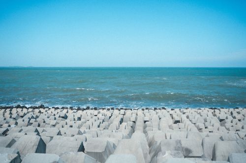 Free A serene seascape with concrete blocks along the coastline against the blue ocean under a clear sky. Stock Photo