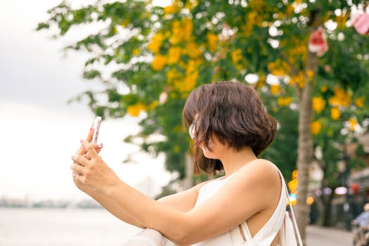 A woman takes a selfie with her smartphone surrounded by vibrant summer foliage, capturing a joyful outdoor moment.