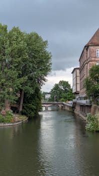 Explore the tranquil canals of Nuremberg under an overcast sky, flanked by historic architecture and lush greenery.