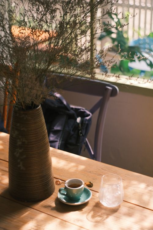 Free Sunlit cafe table with coffee, water, and decorative vase for a relaxing vibe. Stock Photo