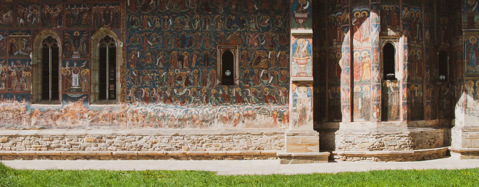 Exterior wall of an ancient monastery adorned with vibrant frescoes under sunny skies.