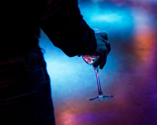 Free Silhouette of a person holding a wine glass against a vibrant nightclub background. Stock Photo