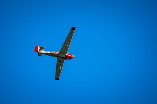 Free A small red and white airplane flying against a clear blue sky, shot from below in vibrant daylight. Stock Photo