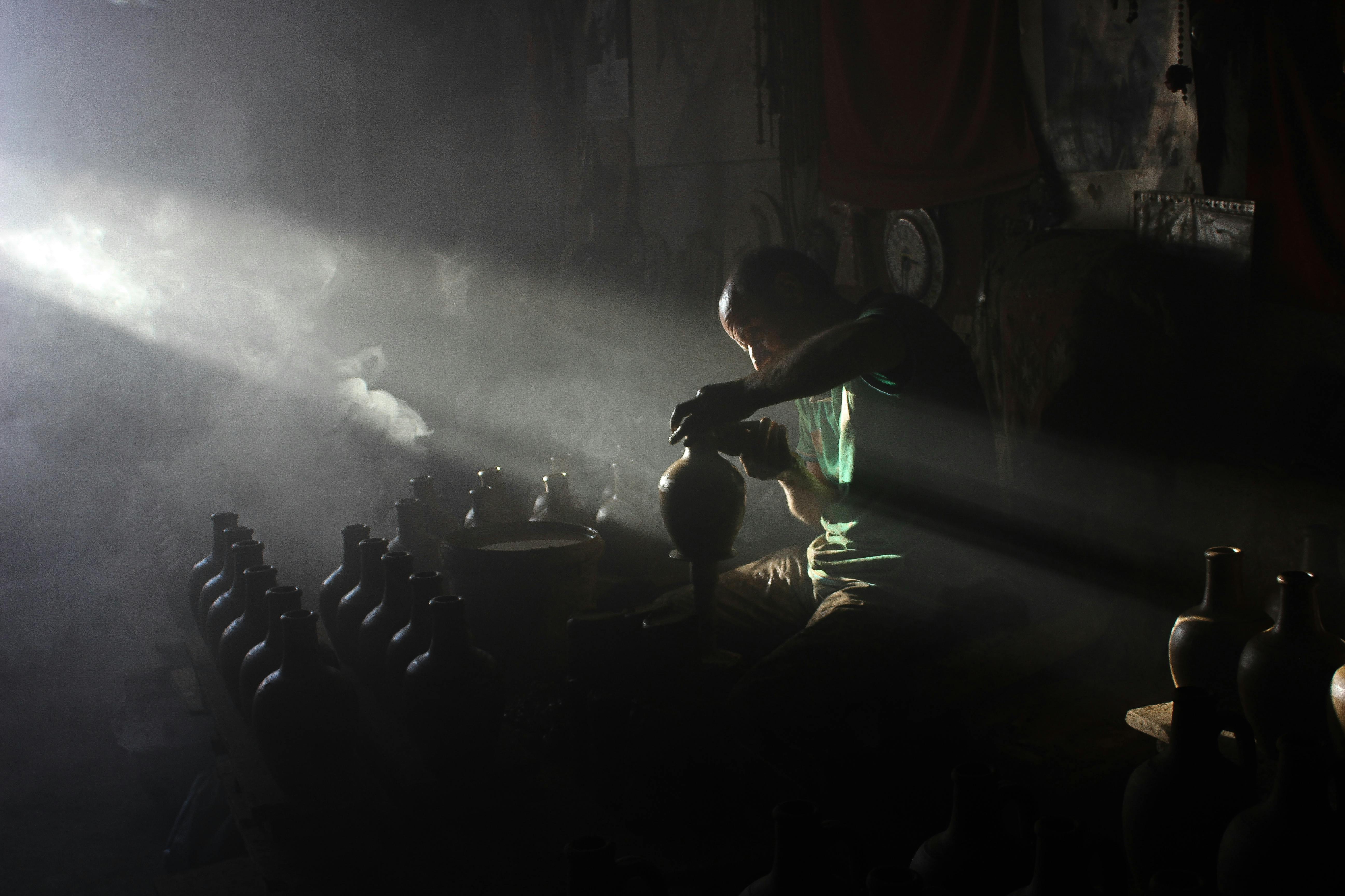 Gratuit Un meșteșugar modelează cu măiestrie un oal de lut sub o lumină atmosferică într-un atelier de olărit. Fotografie de stoc